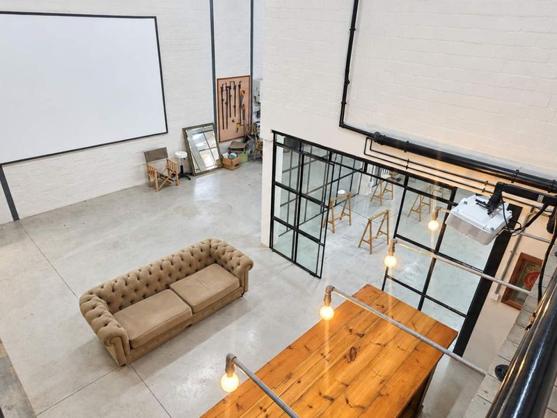 Spacious industrial-style open plan area featuring high ceilings, concrete floors, exposed piping, and a large steel-framed glass partition overlooking the lower level.