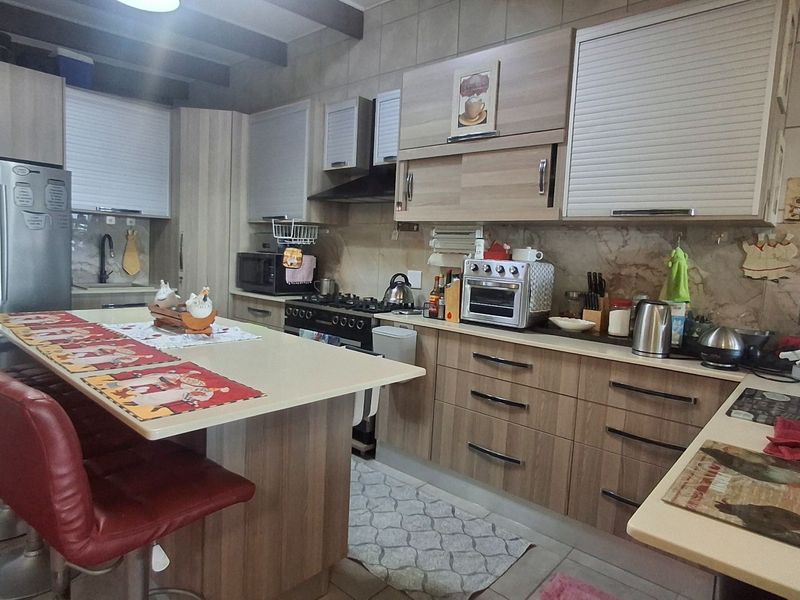 A functional kitchen featuring wood-look cabinetry, a central island, gas hob, extractor fan, and tiled finishes throughout.