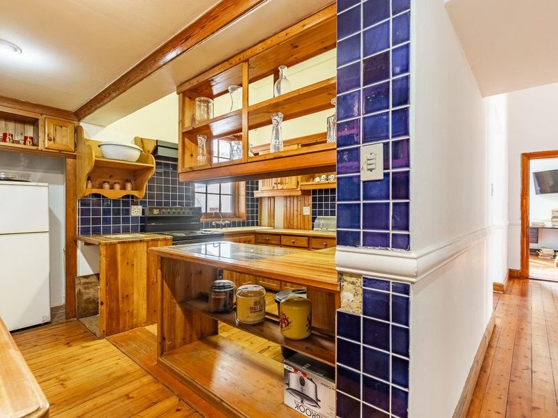 A rustic kitchen featuring wooden cabinetry, blue tiled backsplash, and wooden countertops, with an adjacent view into an office space.