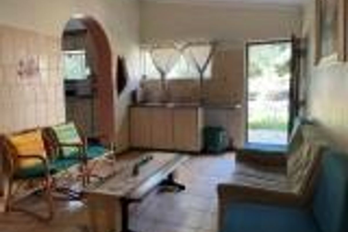 A dated living area featuring tiled flooring, an arched entryway, and a small kitchenette area with built-in cabinetry.