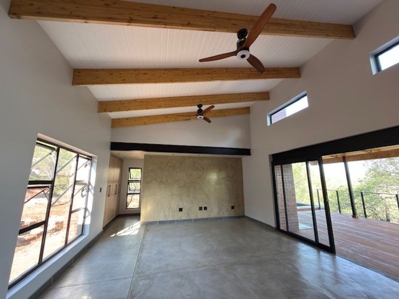 Spacious living area featuring high ceilings with exposed timber beams, polished concrete floors, and large sliding doors opening onto an outdoor deck.