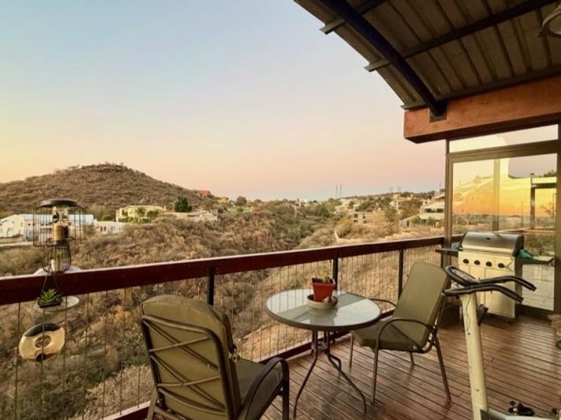 An elevated balcony featuring timber decking and a metal railing, offering expansive views of the surrounding landscape and hills.