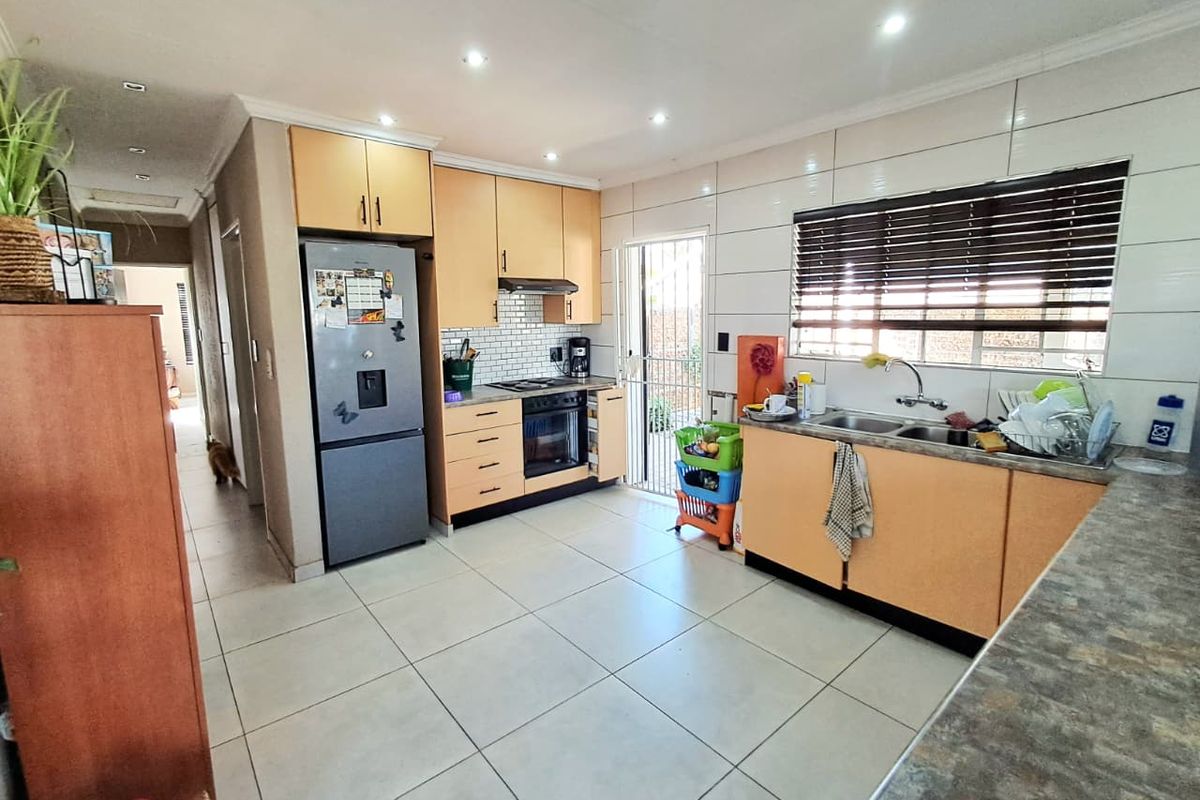 Functional kitchen featuring light wood cabinetry, tiled backsplash, built-in oven and hob, and direct access to the exterior via a security gate.