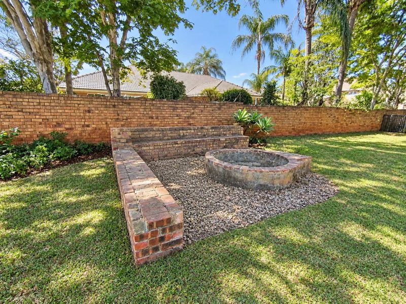A landscaped garden area featuring a built-in brick fire pit with integrated brick seating, surrounded by a mature lawn and brick boundary wall.