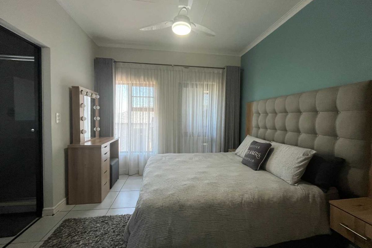 A well-maintained bedroom featuring tiled flooring, a ceiling fan, and a sliding door providing natural light.