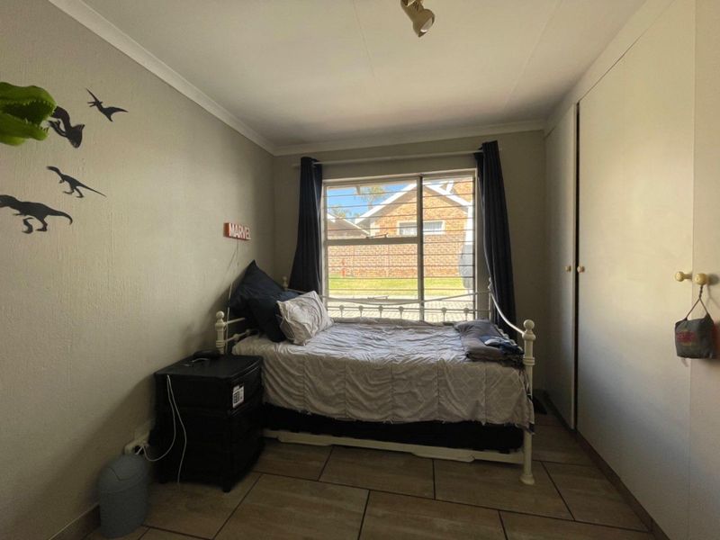A functional bedroom featuring tiled flooring, built-in cupboards, and a window with security bars, providing natural light and storage space.