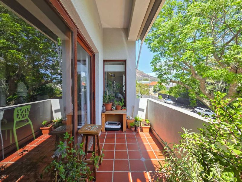 A sunny balcony featuring terracotta floor tiles and a sliding glass door, offering a pleasant outdoor space with views of the surrounding neighborhood.