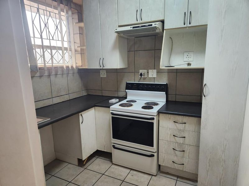 Compact kitchen featuring built-in cabinetry, a freestanding electric stove with extractor fan, tiled backsplash, and tiled flooring.