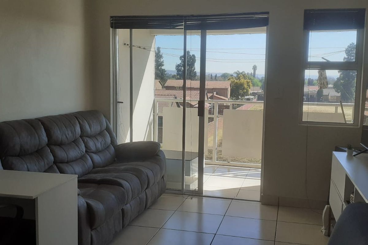 A living room featuring tiled flooring, large sliding glass doors leading to a balcony, and natural light through aluminium-framed windows.