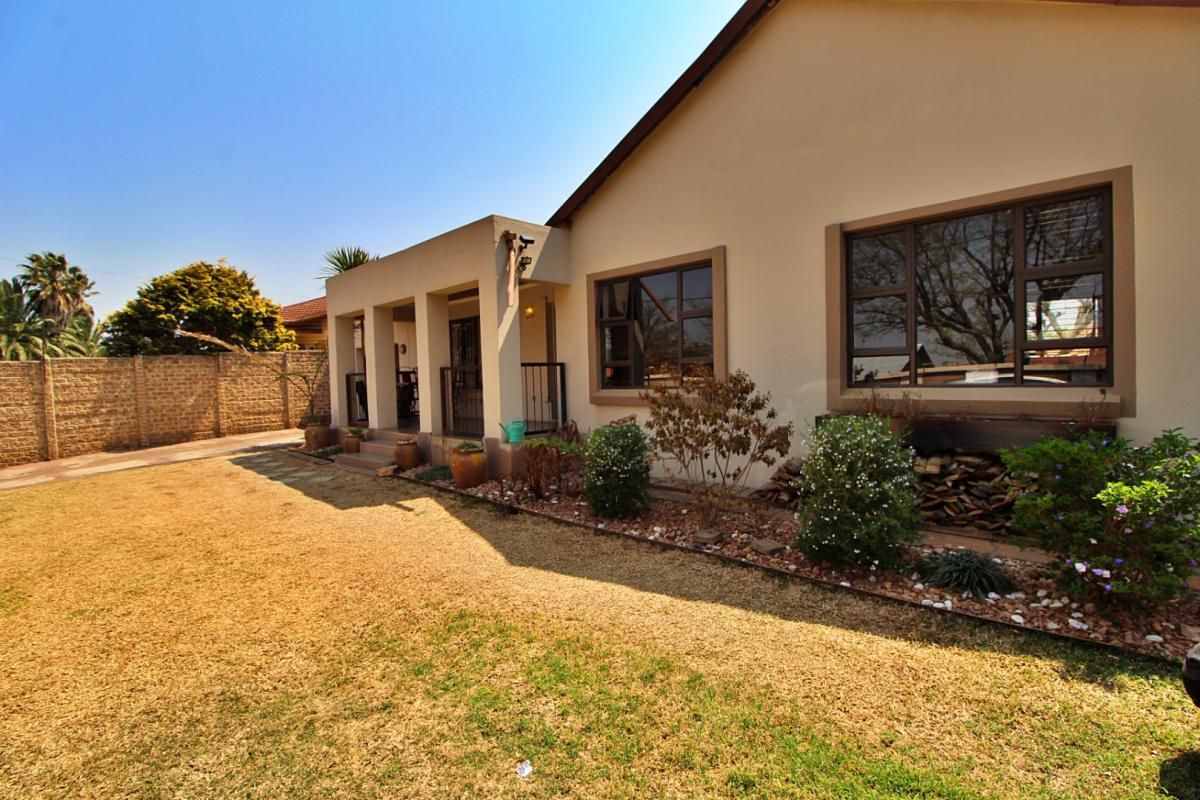 Rear view of the property featuring a covered patio, landscaped garden, and brick boundary wall with aluminium window frames.