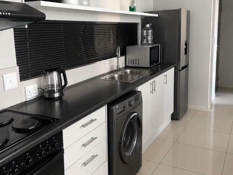 Modern galley-style kitchen featuring white cabinetry, dark countertops, integrated washing machine, and built-in electric stove with extractor fan.