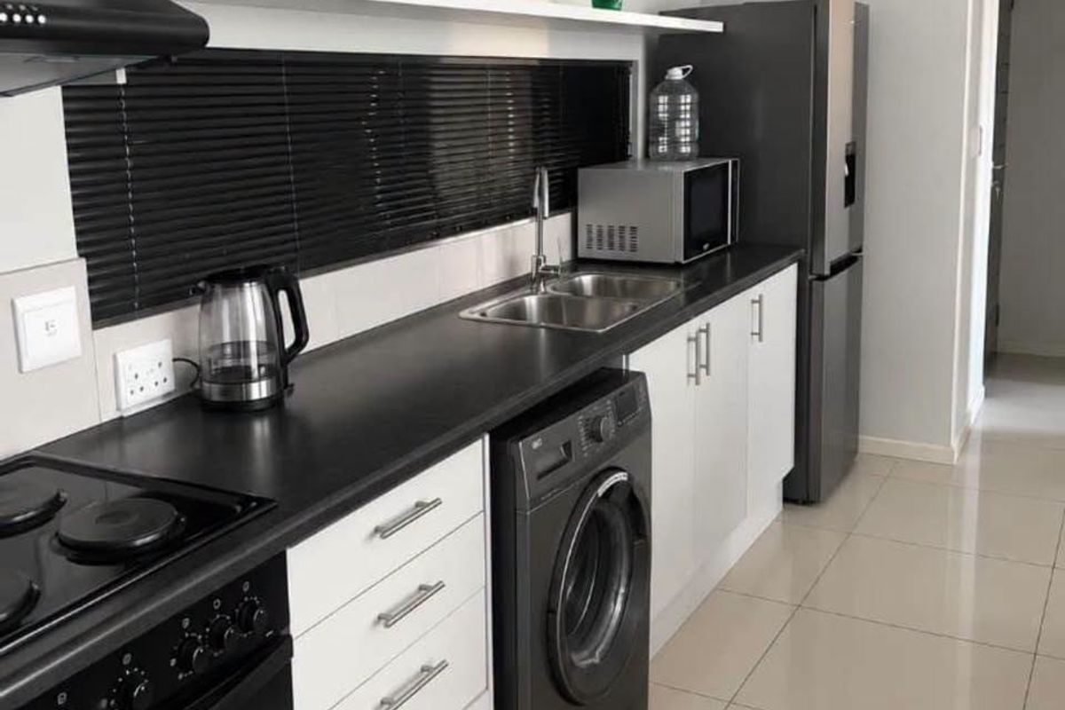 Modern galley-style kitchen featuring white cabinetry, dark countertops, integrated washing machine, and built-in electric stove with extractor fan.