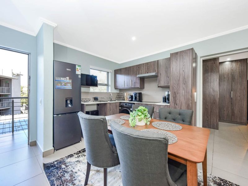 Modern open-plan kitchen and dining area featuring contemporary cabinetry, tiled flooring, and direct access to a private balcony.
