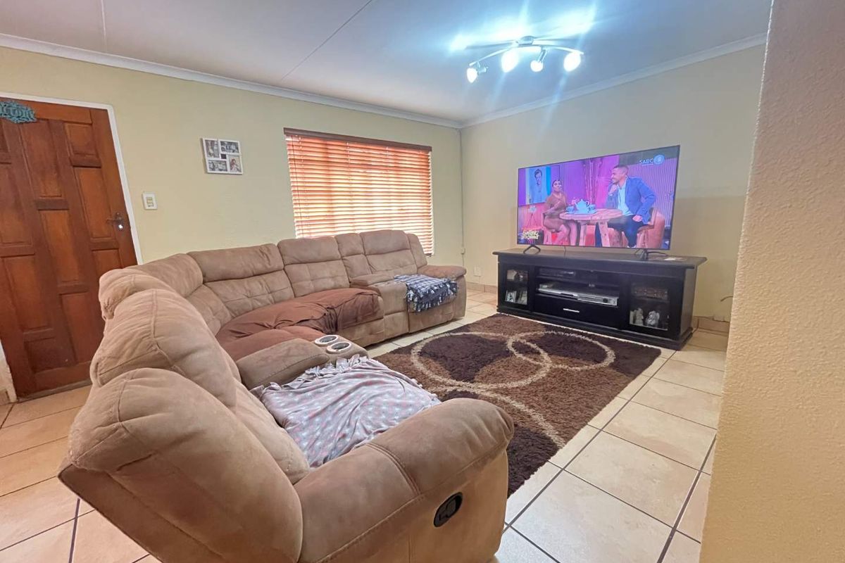 A comfortable living room featuring tiled flooring, a wooden entrance door, and venetian blinds, providing a functional and well-lit space for relaxation.
