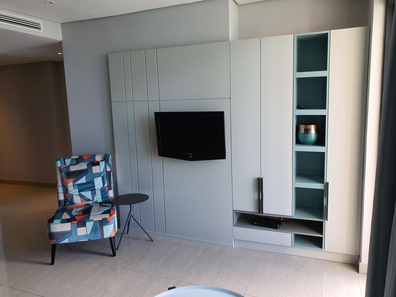 A modern living area featuring custom built-in cabinetry with integrated shelving and a wall-mounted television unit, complemented by neutral tiled flooring.