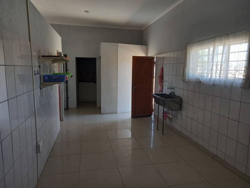 A functional scullery or utility area featuring tiled walls, tiled flooring, and a wall-mounted stainless steel sink.