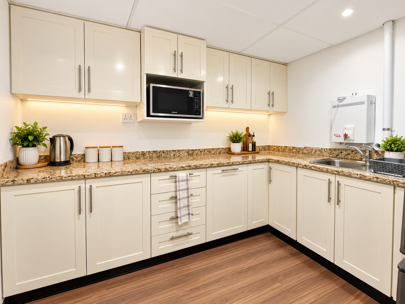 A clean, modern kitchenette featuring cream shaker-style cabinetry, granite countertops, integrated microwave, and a wall-mounted water heater.