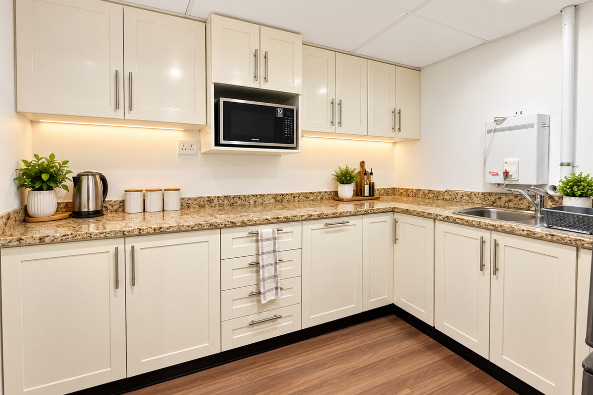 A clean, modern kitchenette featuring cream shaker-style cabinetry, granite countertops, integrated microwave, and a wall-mounted water heater.