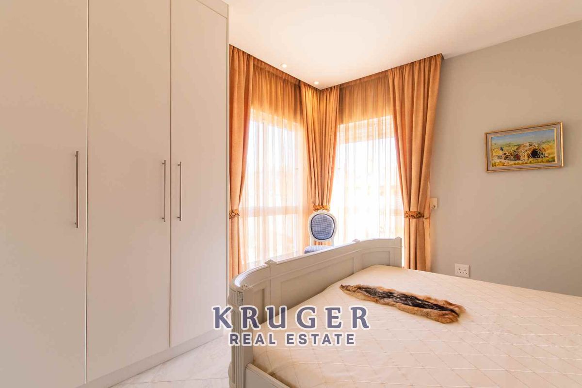 A well-maintained bedroom featuring built-in floor-to-ceiling wardrobes and large windows with elegant curtains, providing ample natural light.