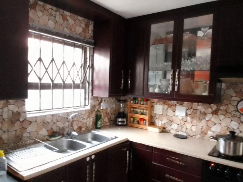 A functional kitchen featuring dark wood cabinetry, stone-look tile backsplash, and a double basin stainless steel sink with chrome fixtures.