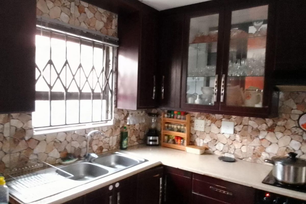 A functional kitchen featuring dark wood cabinetry, stone-look tile backsplash, and a double basin stainless steel sink with chrome fixtures.