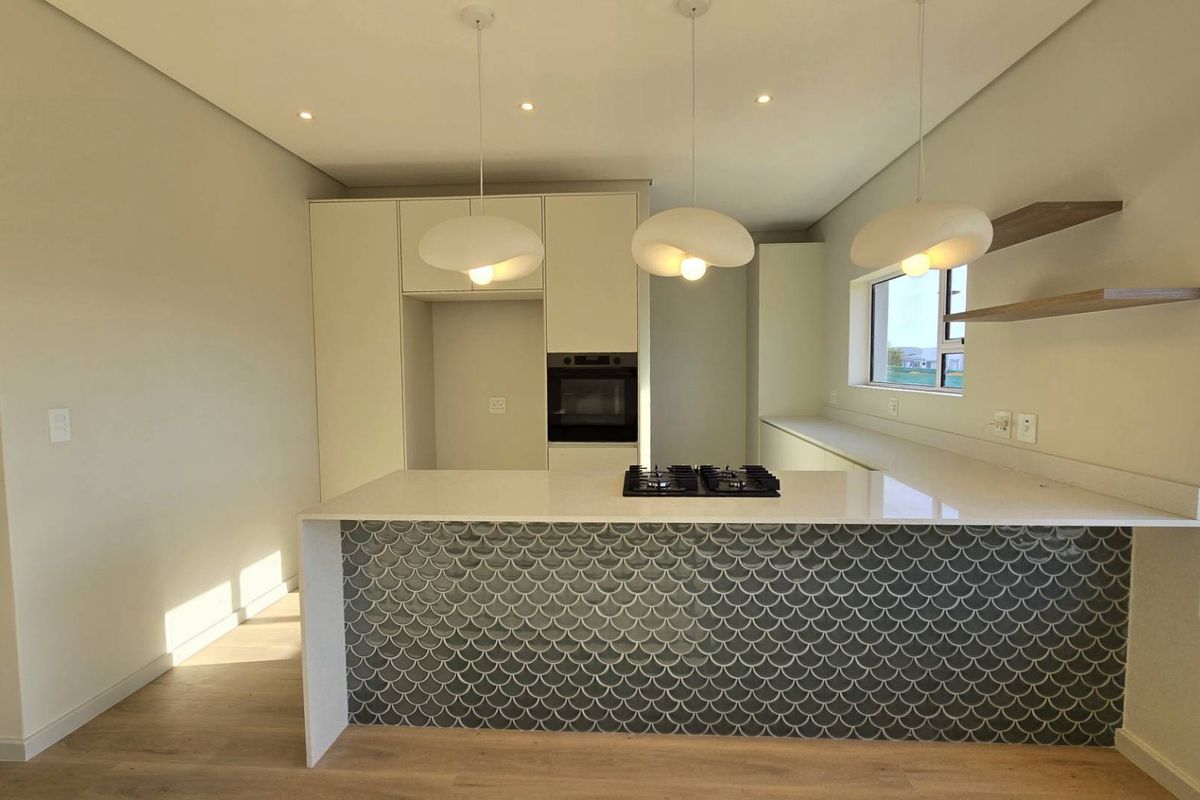 Modern kitchen featuring a striking scalloped tile island, stone countertops, built-in oven, gas hob, and elegant pendant lighting in a bright, open-plan space.
