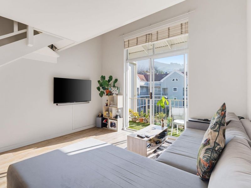 Bright living room featuring laminate flooring, a staircase, and large sliding glass doors opening onto a private balcony.