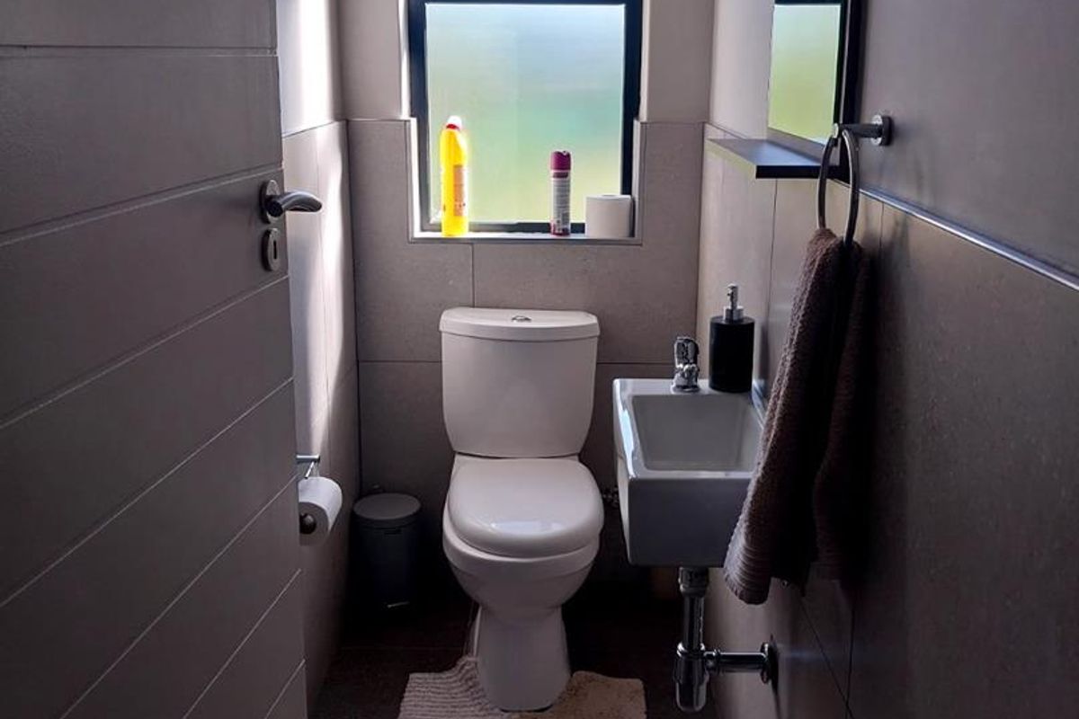 A compact guest bathroom featuring modern floor-to-ceiling tiling, a wall-mounted basin with chrome plumbing, and a white toilet.