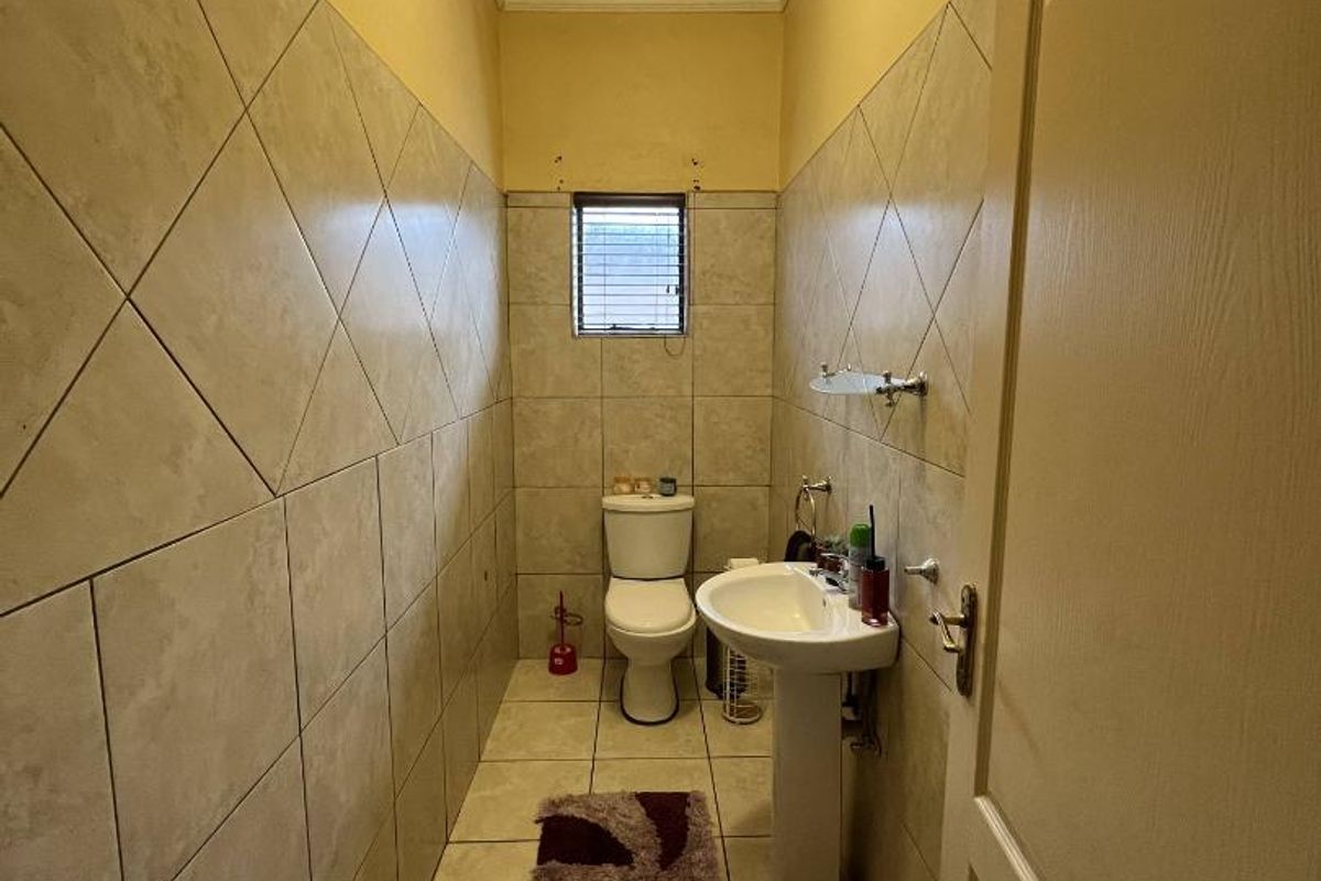 A compact guest bathroom featuring floor-to-ceiling wall tiles, a pedestal sink, and a standard toilet.