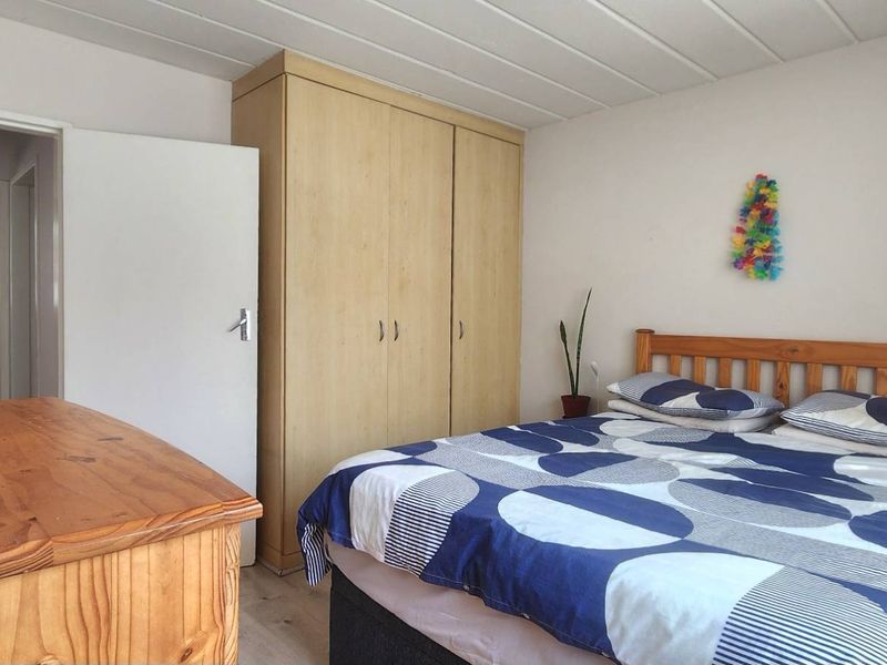 A functional bedroom featuring built-in wooden wardrobes, laminate flooring, and a panelled ceiling, with direct access to an adjoining bathroom.
