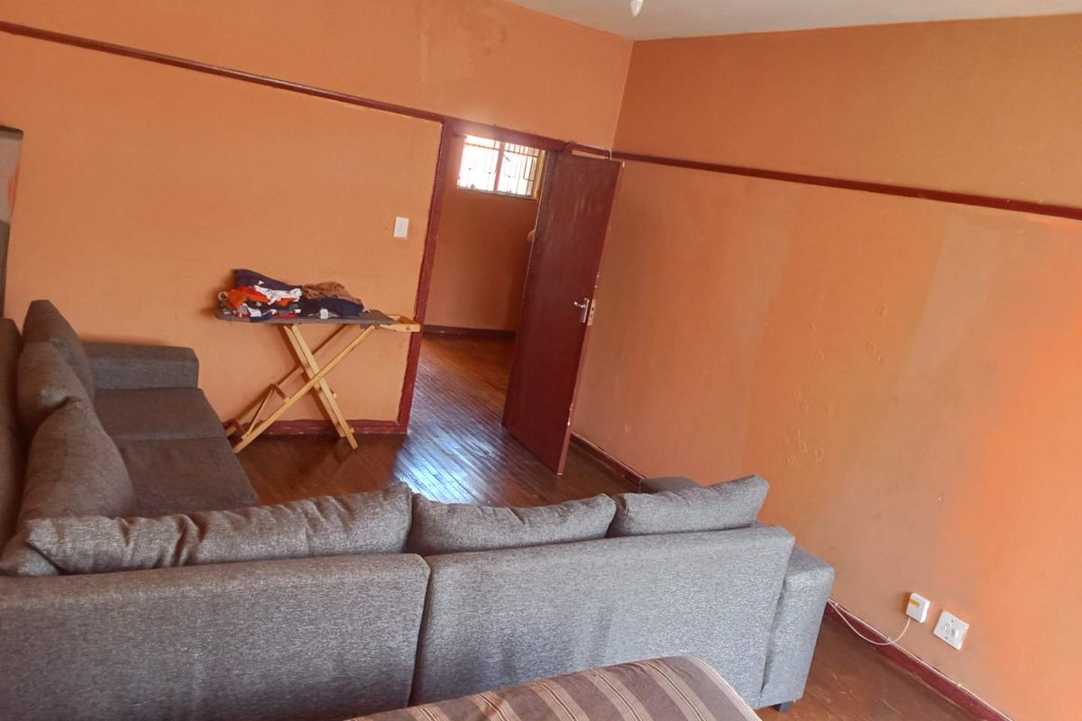 A living room featuring original timber flooring, picture rails, and access to an adjoining room through a wooden door.