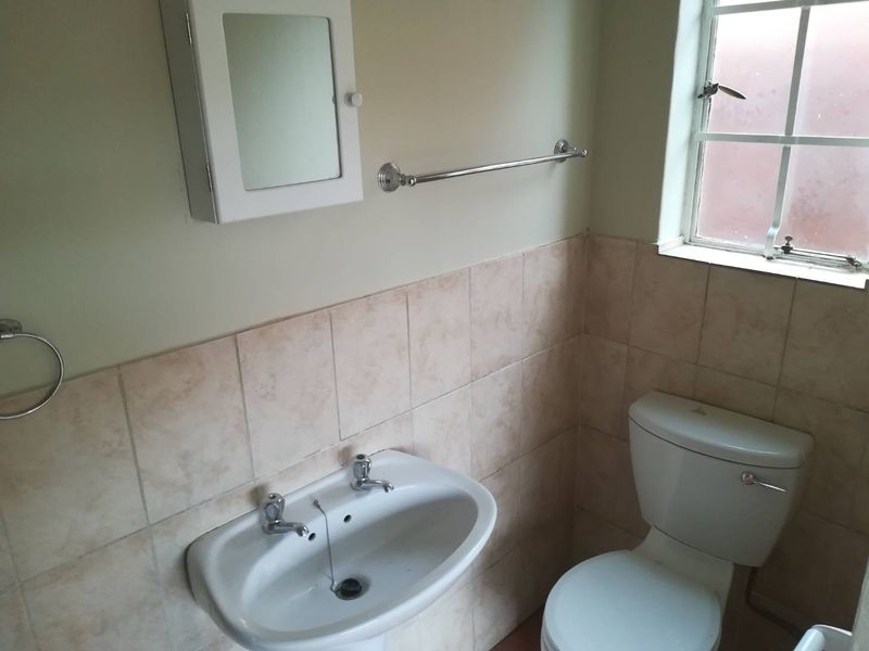 A functional bathroom featuring a pedestal sink, toilet, tiled splashback, and wall-mounted storage cabinet, providing a clean and practical space.