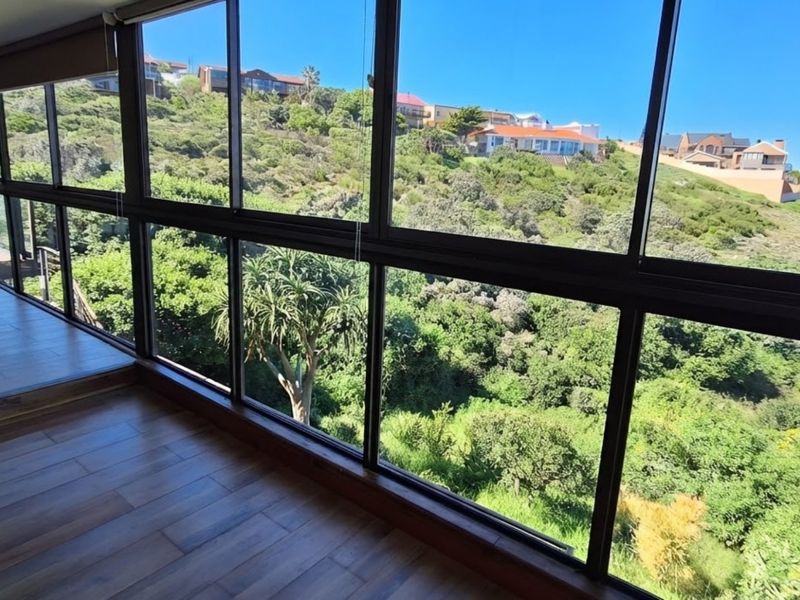 Enclosed balcony featuring expansive glass windows with scenic hillside views and durable laminate flooring.