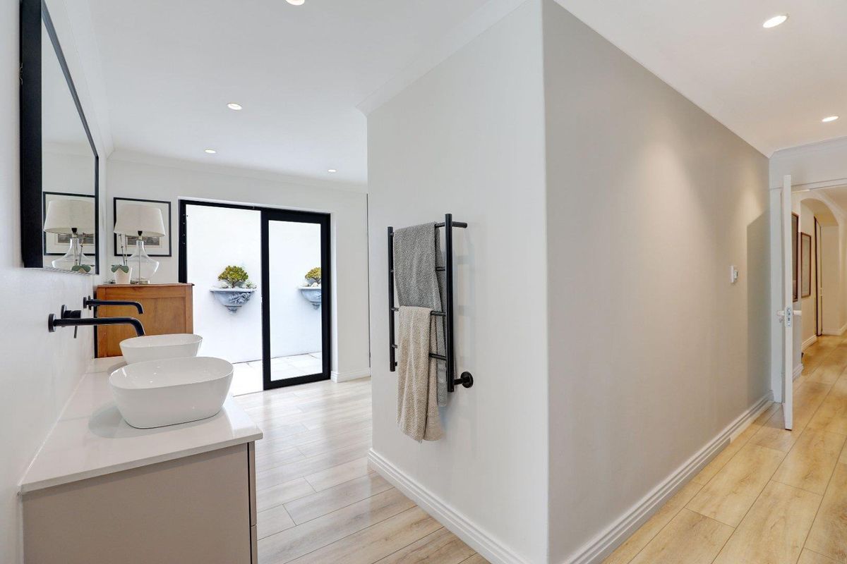 Modern bathroom featuring dual vessel sinks, wall-mounted matte black faucets, a heated towel rail, and direct access to a private outdoor courtyard.