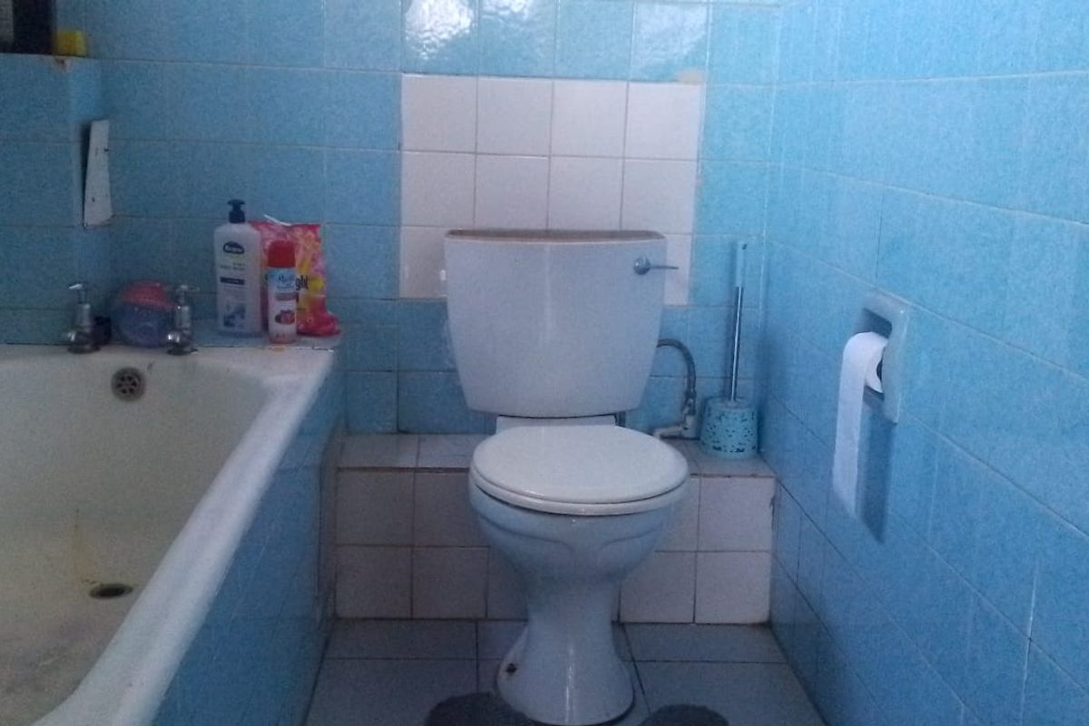 A dated bathroom featuring blue wall tiles, a standard bathtub, and a white toilet suite.