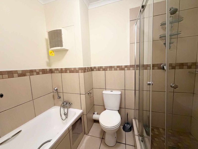 A functional bathroom featuring a bathtub, separate shower enclosure, and toilet with neutral wall and floor tiling.
