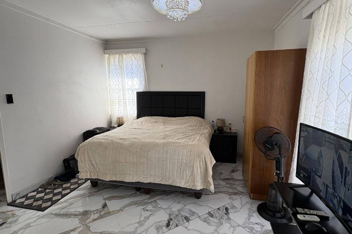 Spacious bedroom featuring large-format marble-look floor tiles and a decorative crystal chandelier, offering a bright and neutral foundation for personal styling.