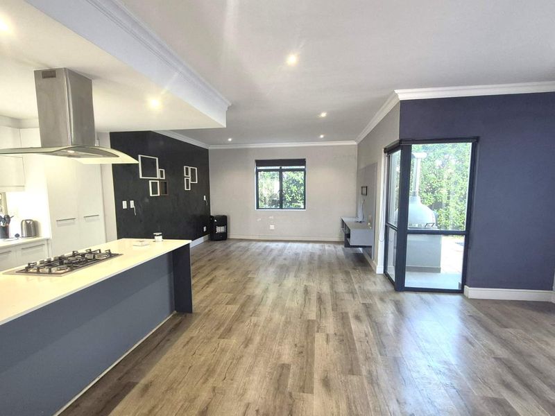 Spacious open-plan living area featuring a modern kitchen with a central island, gas hob, and sleek laminate flooring, leading to an outdoor patio space.