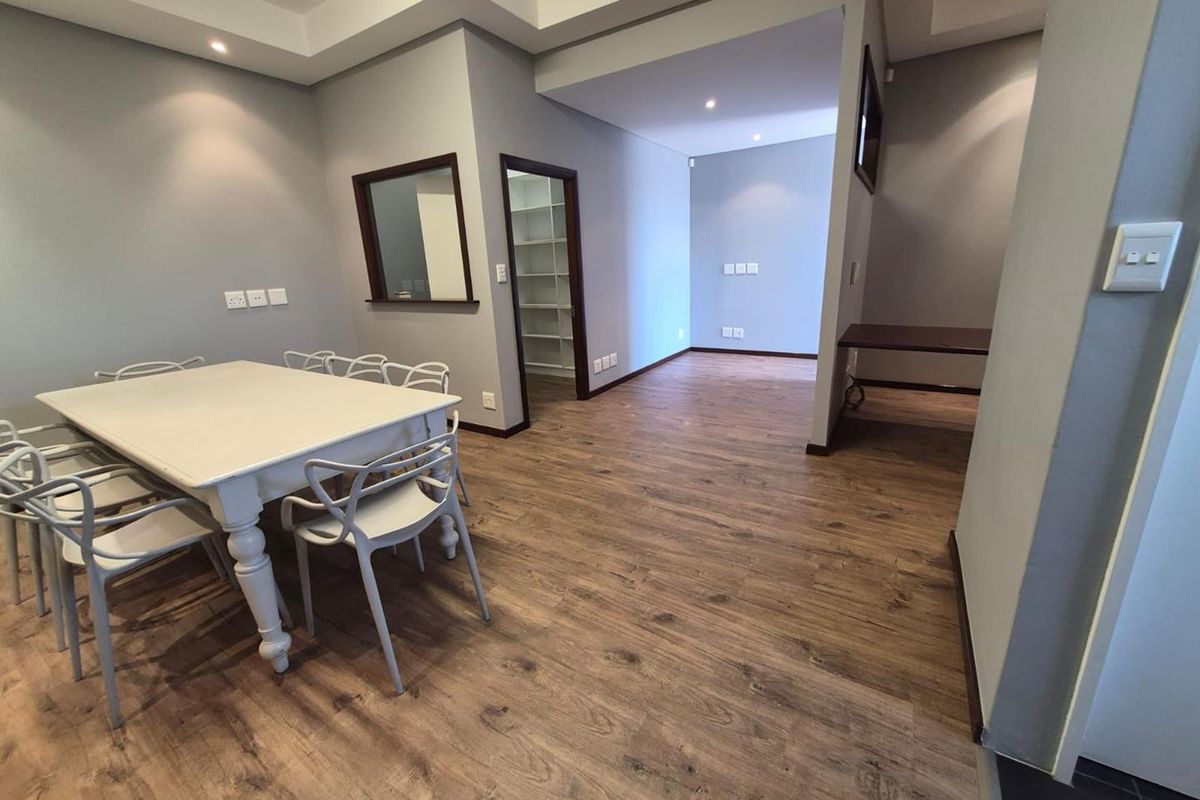 A modern office space featuring durable laminate flooring, recessed lighting, and a convenient pass-through window connecting to an adjacent room.