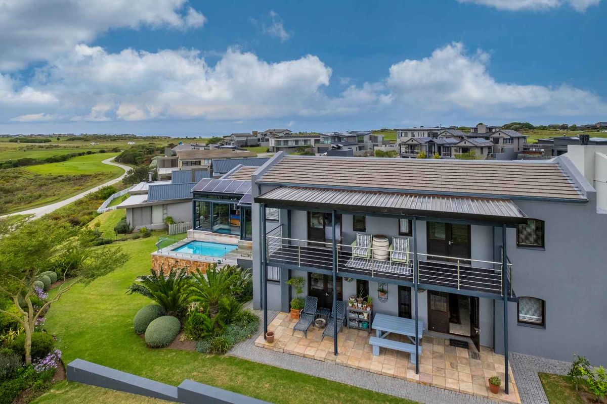 Aerial view of a modern two-story house featuring a tiled roof, a swimming pool, a covered patio, and a balcony overlooking a landscaped garden.