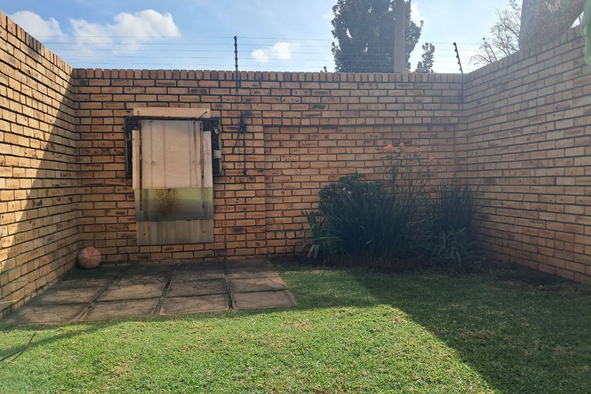A private rear courtyard featuring high face-brick boundary walls with electric fencing, a small lawn area, and a paved section with a boarded-up wall opening.
