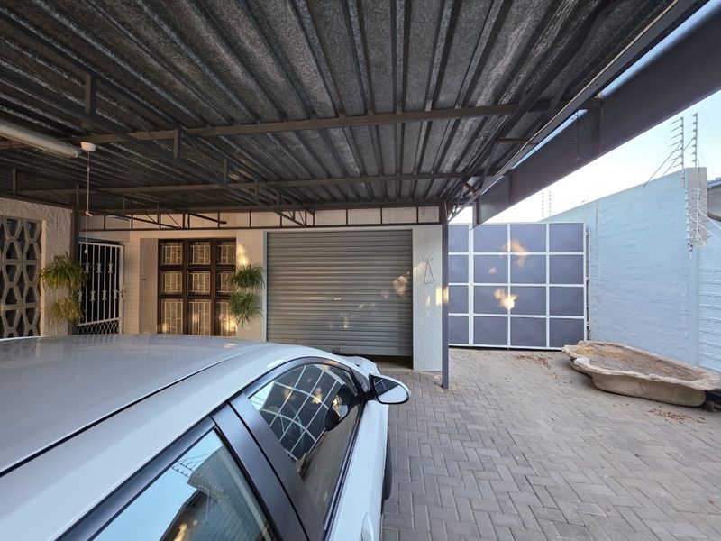 Covered carport area featuring a roller shutter garage door, paved flooring, and secure perimeter walling with electric fencing.