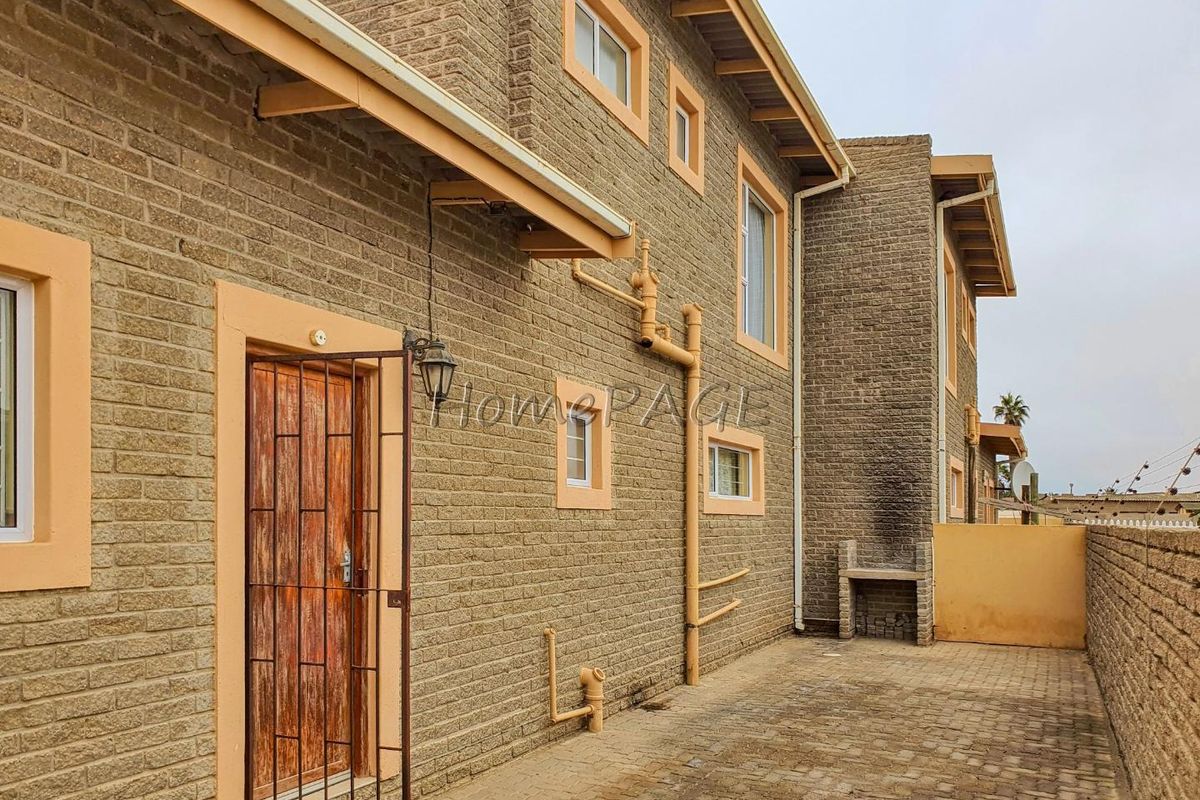 Rear exterior view of the townhouse featuring a paved courtyard, built-in brick braai, and security gate access.