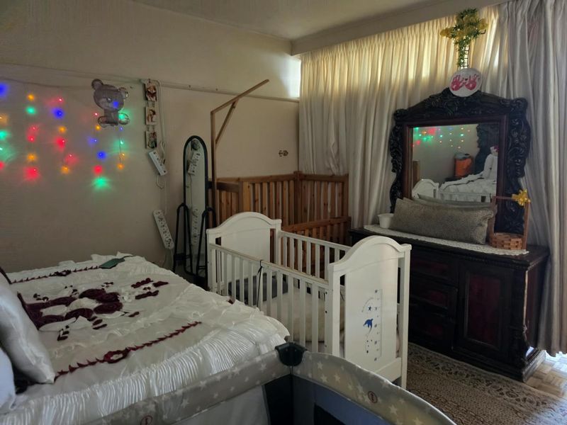A bedroom featuring parquet flooring and full-length window curtains, currently utilized as a nursery with multiple cribs and bedroom furniture.