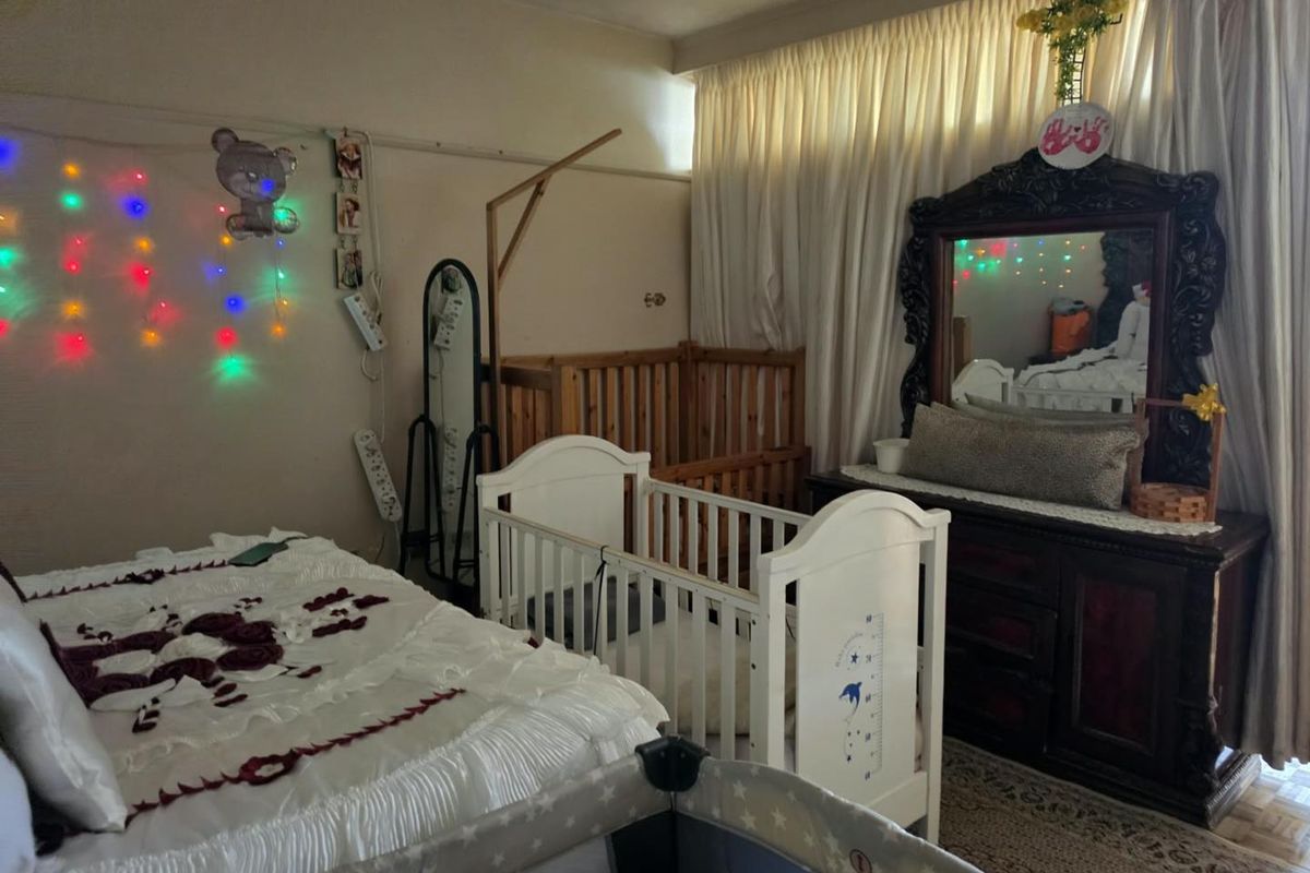 A bedroom featuring parquet flooring and full-length window curtains, currently utilized as a nursery with multiple cribs and bedroom furniture.