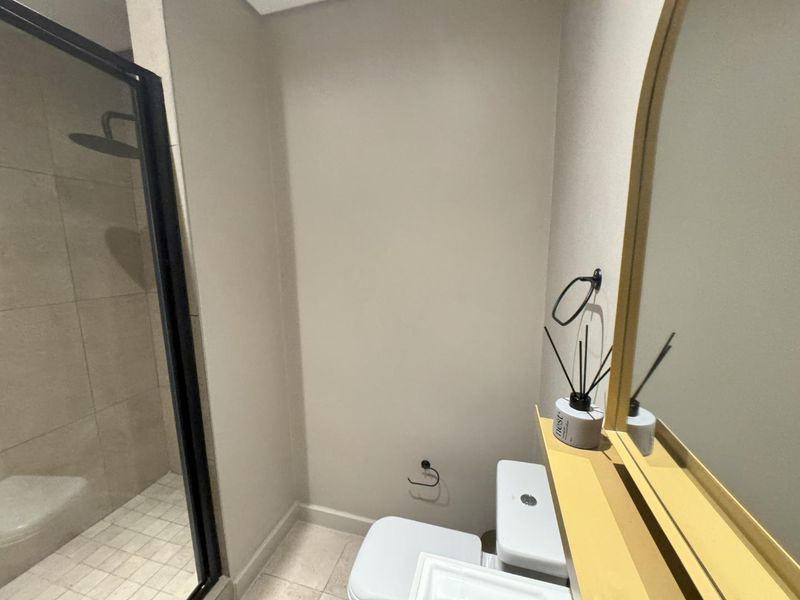 A modern bathroom featuring a glass-enclosed shower, tiled flooring, and a wall-mounted mirror with a shelf.
