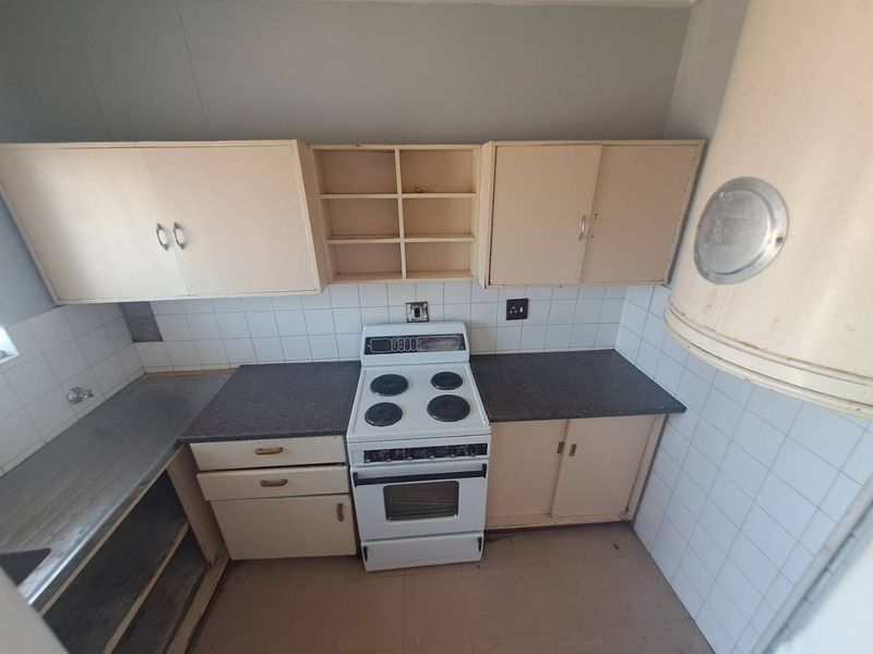 A dated kitchen featuring original cabinetry, a freestanding electric stove, tiled backsplash, and a stainless steel sink, offering significant potential for modernization.