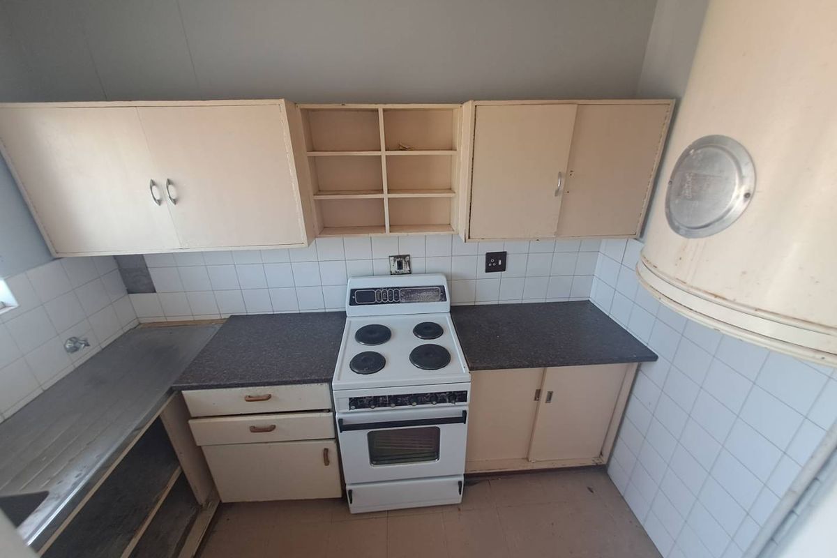 A dated kitchen featuring original cabinetry, a freestanding electric stove, tiled backsplash, and a stainless steel sink, offering significant potential for modernization.