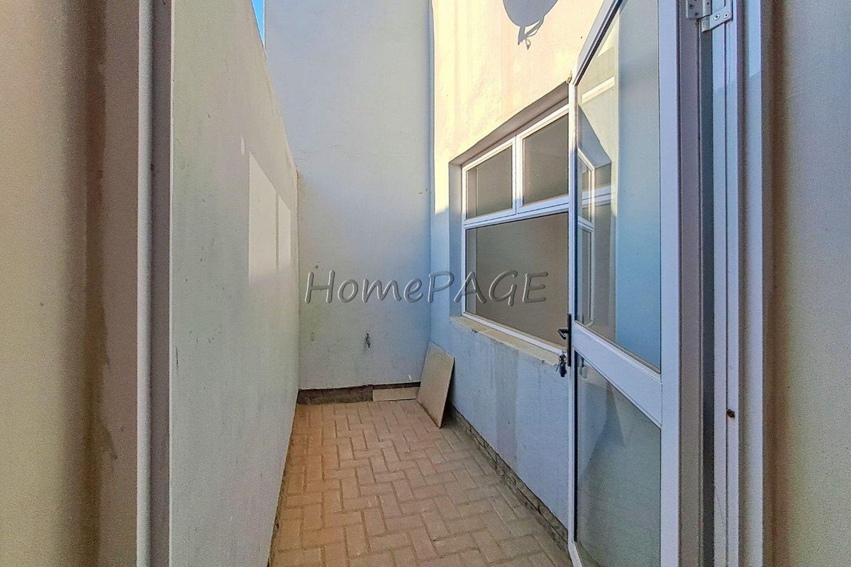A narrow exterior side passage or courtyard featuring paved flooring and access via a glass-paneled door.