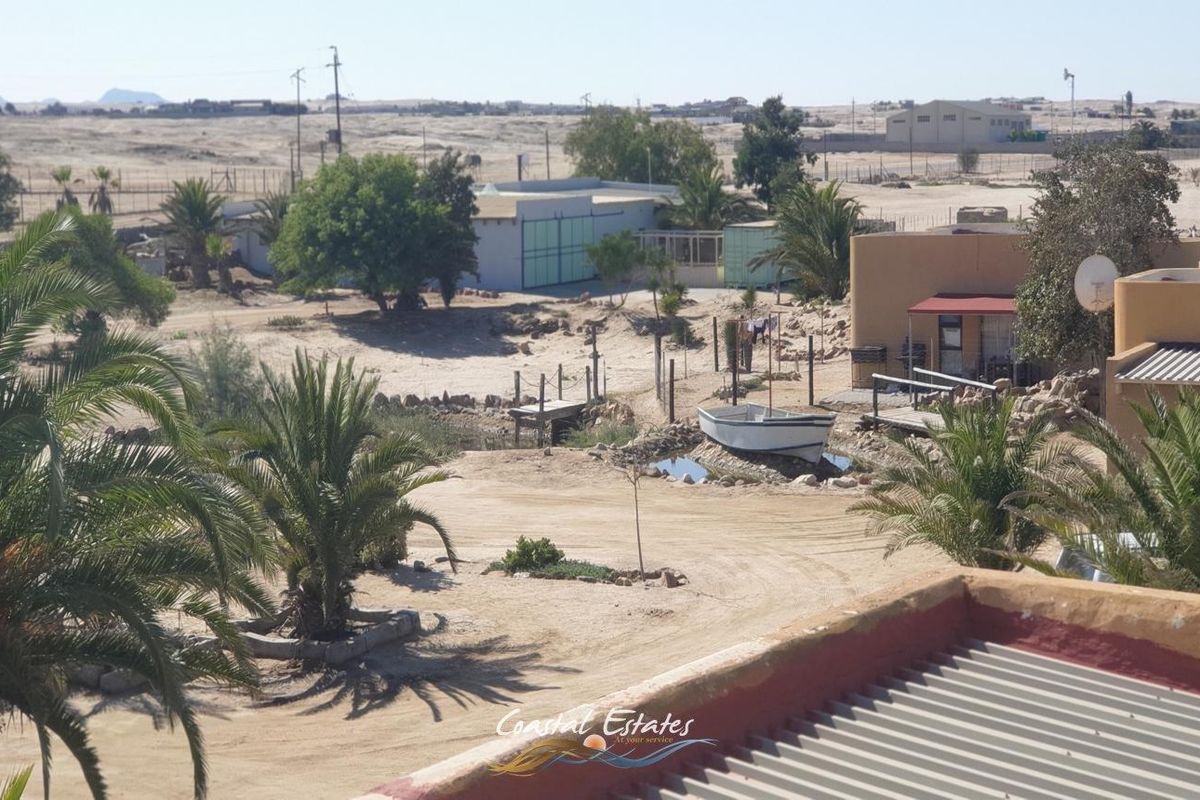 Aerial view of the small holding property grounds, featuring outbuildings, sandy landscape, and established palm trees under a clear sky.
